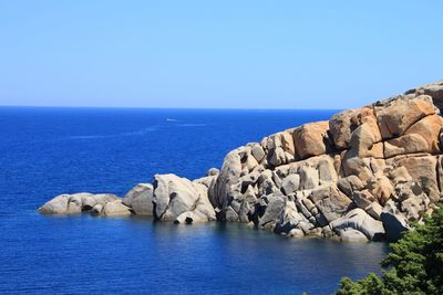Rocks by sea against clear blue sky