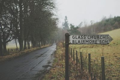 Sign on road by trees against sky