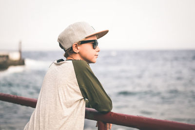 Man looking away while standing by railing against sea