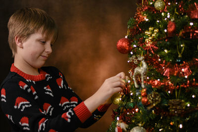 Side view of boy decorating christmas tree at home