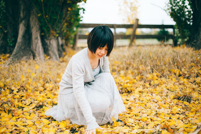 Woman collecting leaves while crouching at park
