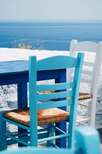 Empty chairs and table by sea against sky