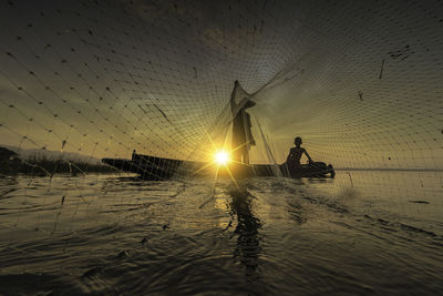 Fisherman with boy holding fishing net in boat on sea during sunset