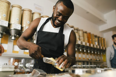 Smiling young owner filling food in jar while working in store