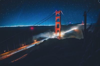 High angle view of light trails on suspension bridge against star field