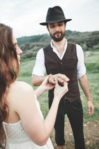 Bride inserting wedding ring in groom finger on field