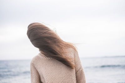 Woman with brown hair covering face against sea at beach