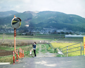 Woman photographing while standing on land against mountains and sky