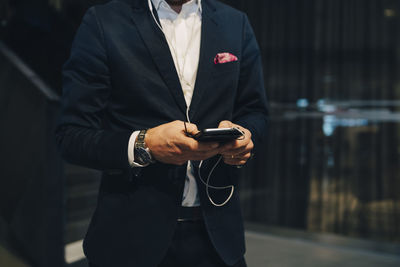 Midsection of businessman using smart phone with headphones in office