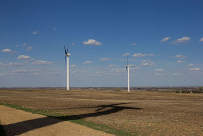 Two wind turbines with the shadow of a wind turbine on the ground.