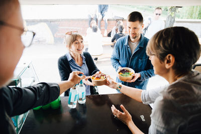 Mature owners serving food and drink to happy customers while standing in commercial land vehicle