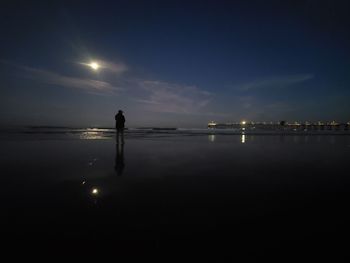 Silhouette man standing at beach against sky at night