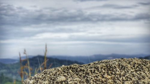 Close-up of cliff against cloudy sky