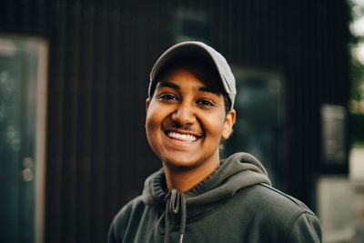 Portrait of smiling man wearing cap and hooded shirt at city