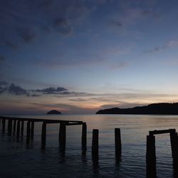 Wooden posts in sea against sky during sunset