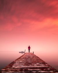 Man standing on pier over sea against sky during sunset