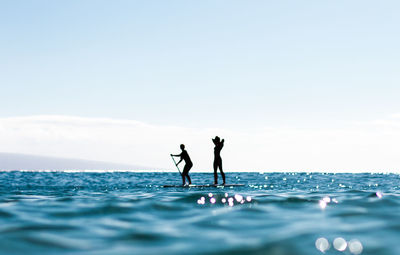 Silhouette women on raft at sea against sky