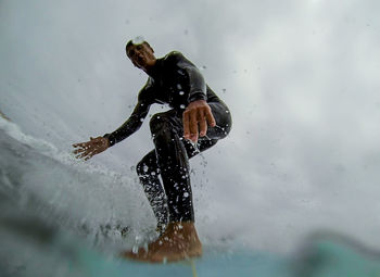 Low angle view of mature man surfing on sea against cloudy sky