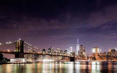 Manhattan bridge over east river by illuminated cityscape at night