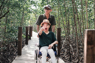 Father with disabled boy on wheelchair against trees