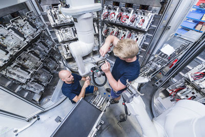 Two colleagues working at industrial robot in modern factory