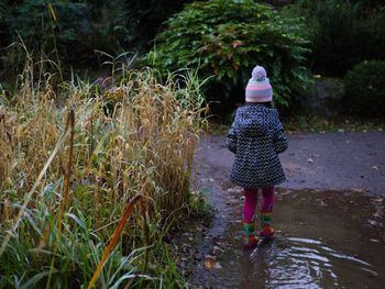 Rear view of young girl walking in the muddy puddle 