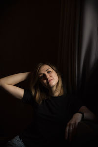 Portrait of beautiful young woman sitting against black background