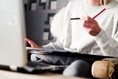 Midsection of woman holding pencil while sitting at home