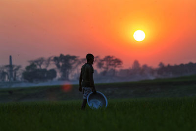 Rear view of man on field against sky during sunset