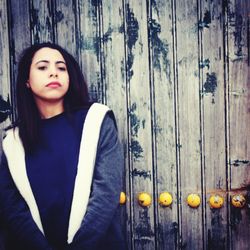 Portrait of a beautiful young woman standing against wooden wall