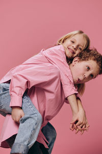 Playful boy giving piggyback ride to sister against pick background