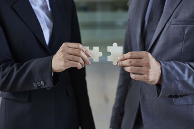 Midsection of business people holding jigsaw pieces at office