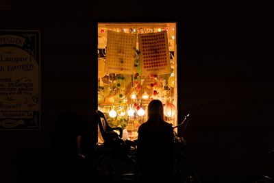 Rear view of people sitting in illuminated building at night