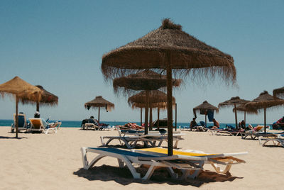 Lounge chairs and parasols on beach against clear sky