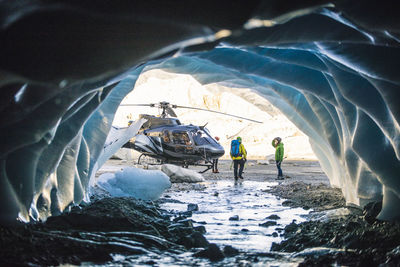 Couple approaches helicopter after exploring ice cave.