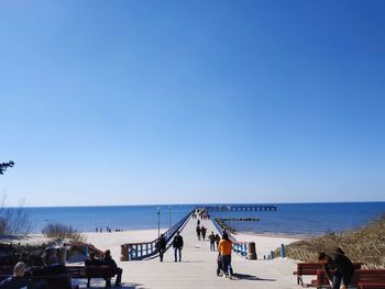 People on beach against clear blue sky