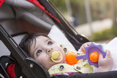 Cute toddler sulking pacifier while looking away in baby stroller outdoors