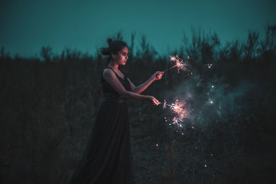 Woman with arms outstretched standing on field at night