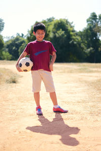 Smiling boy holding soccer ball while standing on field