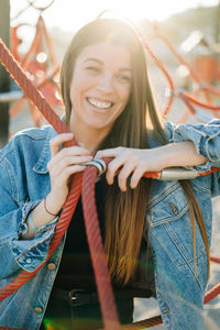 Thoughtful young woman smiling while standing amidst ropes at playground