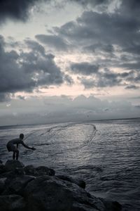Man standing in sea against sky during sunset
