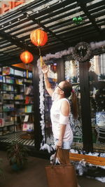 Side view of woman touching lantern hanging in store