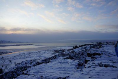 Snow covered land and sea against sky during sunset