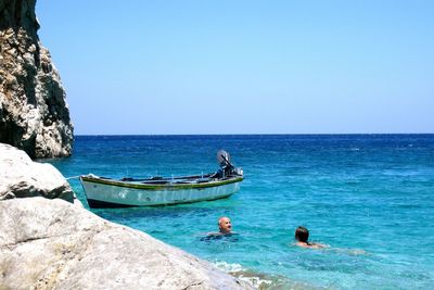 Man and girl swimming by boat in sea against clear sky on sunny day