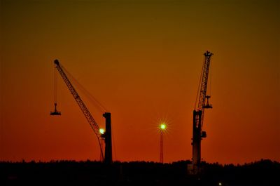 Silhouette cranes at construction site against sky during sunset