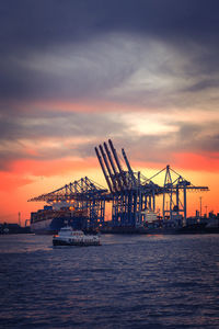 Cranes at commercial dock against sky during sunset