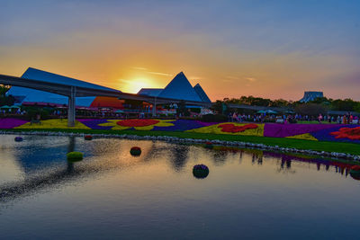 Scenic view of lake by buildings against sky during sunset