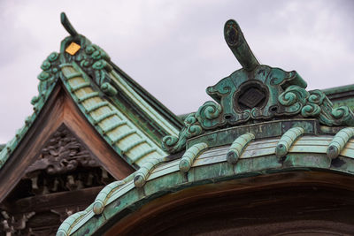 Low angle view of roof tiles and decoration on japanese temple against sky