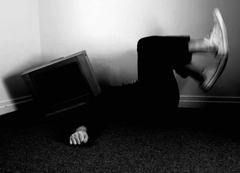 Person face covered by television set while lying on floor against wall