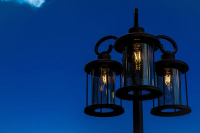 Low angle view of illuminated street light against blue sky